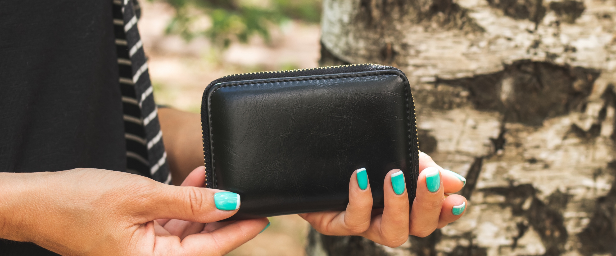 A woman with bright, aqua green nails holds a black leather wallet